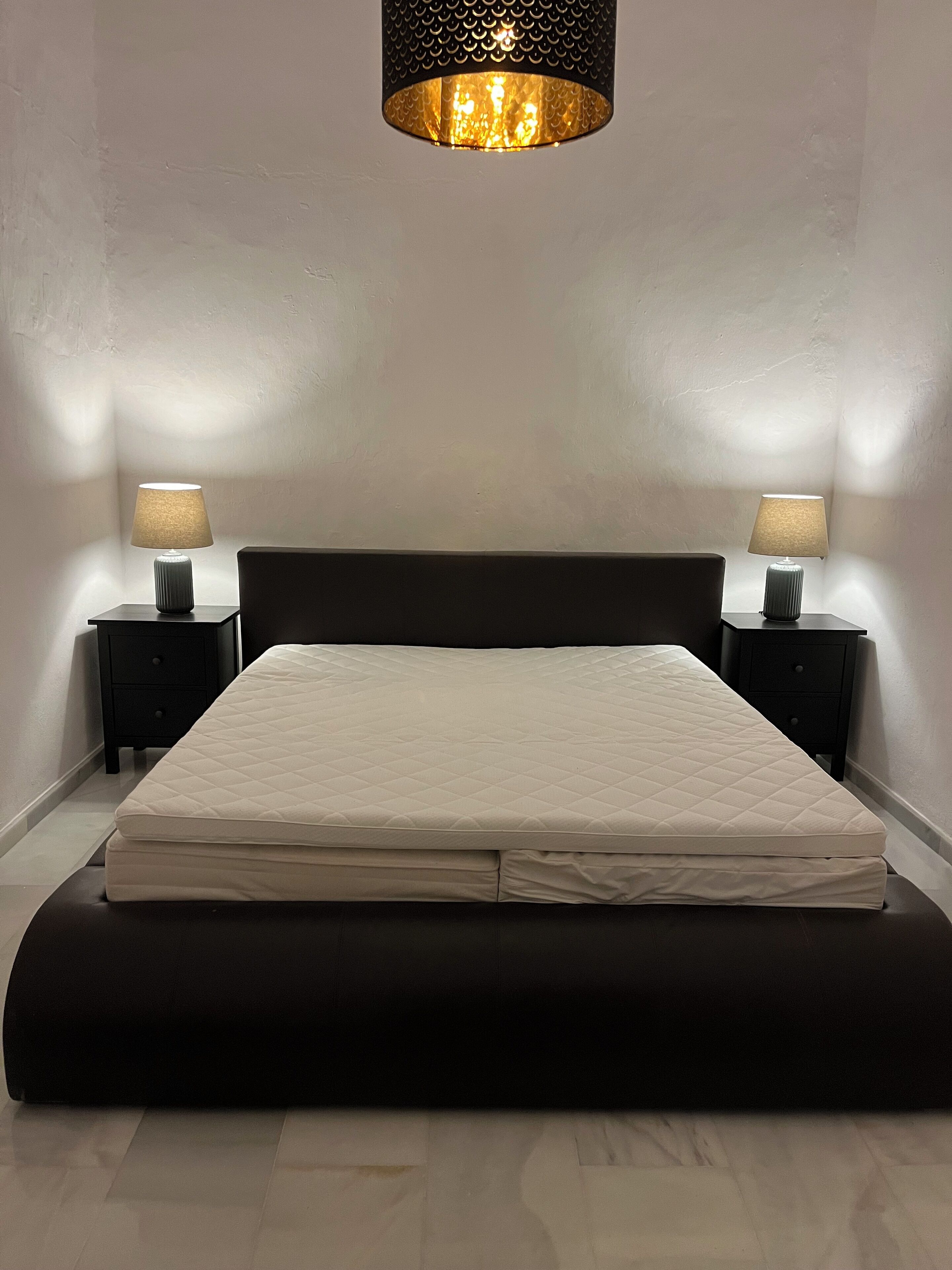 Un lit avec un matelas matelassé, deux tables de chevet avec des lampes et un mur à motifs.