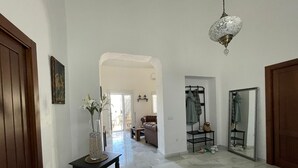 A spacious hallway with a marble floor, a hanging light fixture, and a coat rack.