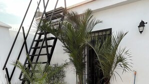 A patio with a round table and chairs, potted plants, a metal staircase, and a black gate.