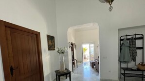 A hallway with a wooden door, a small table with a vase, and a metal rack with clothes.
