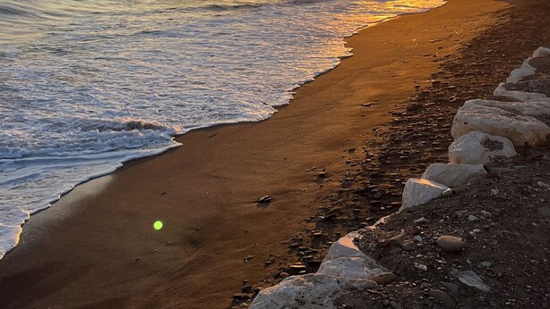 A beach with waves, a sunset, and a rocky shoreline.