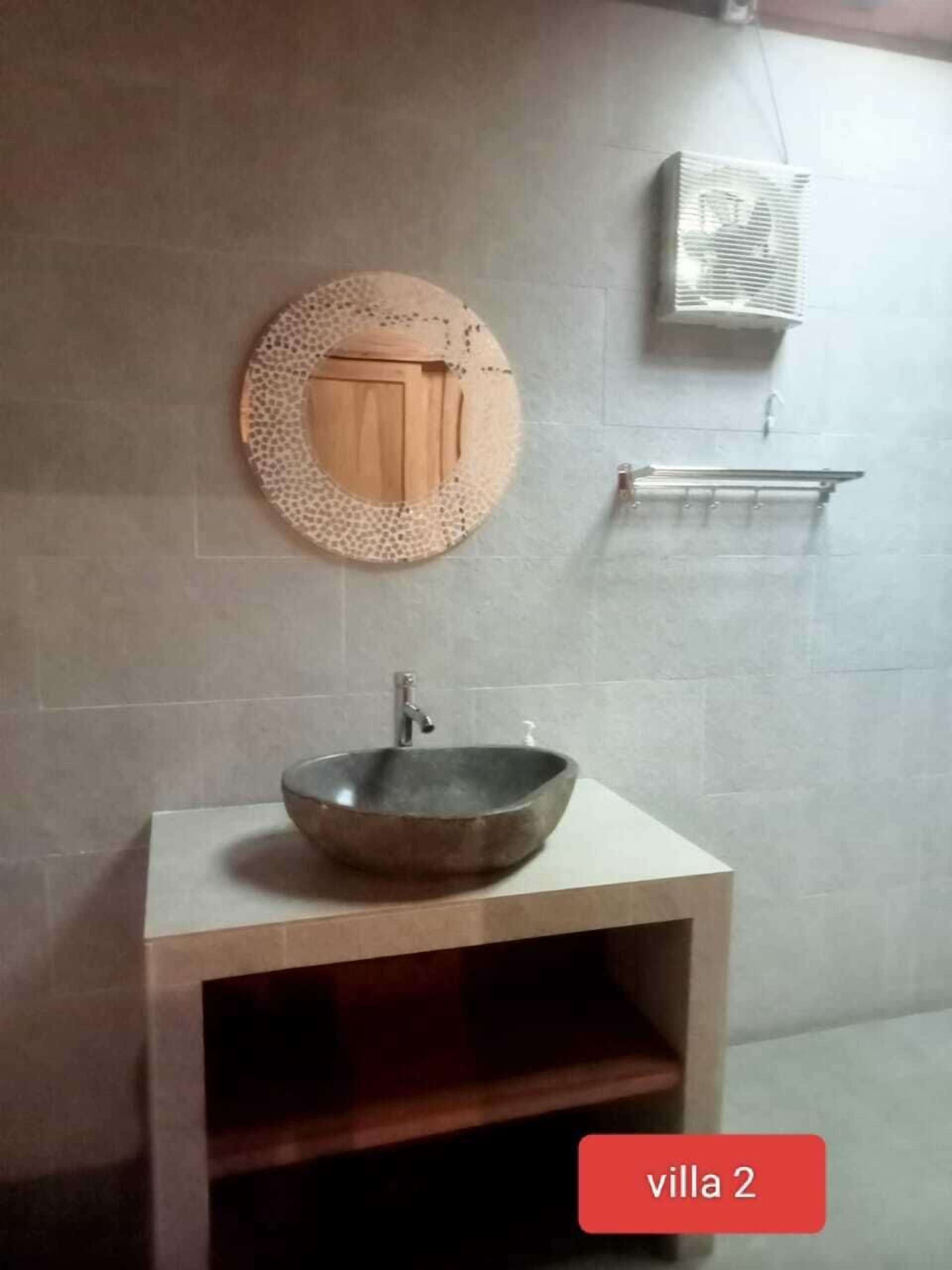 Un baño con un espejo redondo, un mueble de madera, un lavabo tipo recipiente y un perchero para toallas.