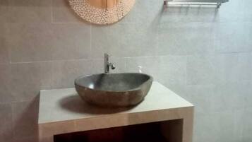 Un baño con un espejo redondo, un mueble de madera, un lavabo tipo recipiente y un perchero para toallas.