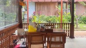 Un espacio de estar techado al aire libre con mobiliario de madera y vistas a un jardín.