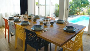 Una mesa de comedor dispuesta con cuencos blancos y azules estampados, copas de vino y cubiertos, con vistas a una piscina y zonas verdes.