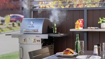 An outdoor dining area with a grill, a plate with a burger, condiments, and a bottle of beer.