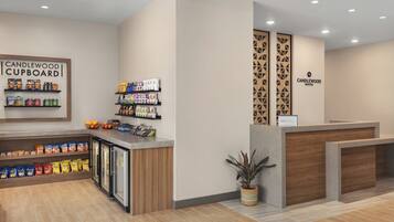 A reception area with a counter, shelves with snacks, a sign for Candlewood Cupboard, and a potted plant.