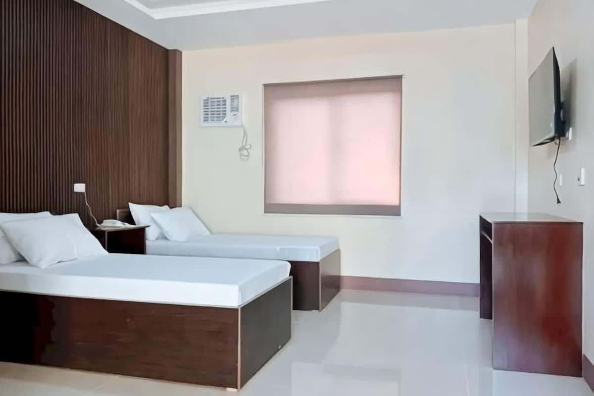 A hotel room with a bed, a desk, a TV, and a window.