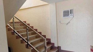 A staircase with a glass railing leading to a landing, a wall-mounted air conditioning unit, and a fire extinguisher on the right. - OYO 1122 Ranchotel Aklan (Kalibo)