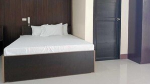 A bedroom with a large bed, a dark wooden headboard, a closed door, and a nightstand with a phone. - OYO 1122 Ranchotel Aklan (Kalibo)