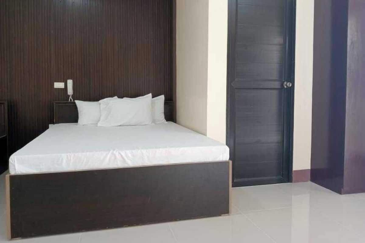 A bedroom with a large bed, a dark wooden headboard, a closed door, and a nightstand with a phone.