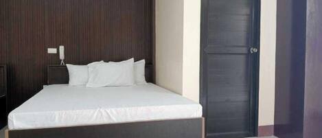 Une chambre à coucher avec un grand lit, une tête de lit en bois foncé, une porte fermée et une table de chevet avec un téléphone.