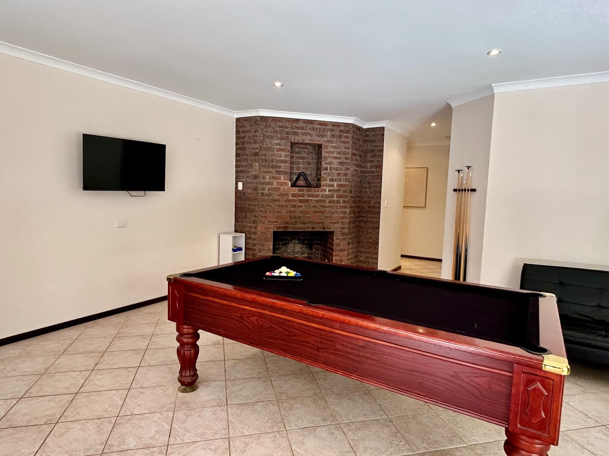 Una mesa de billar en una habitación con chimenea de ladrillo, un televisor en la pared y una puerta que da a otra estancia.