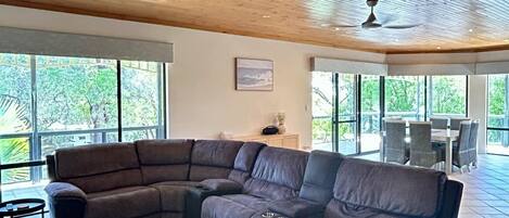 A large L-shaped sectional sofa in a spacious room with a wooden ceiling and large windows.