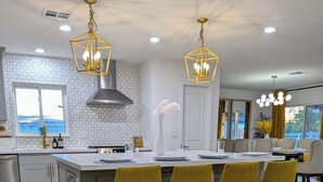 A modern kitchen with a central island, bar stools, pendant lighting, and a view to the outside.