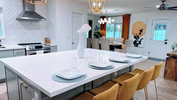 A modern kitchen with a large island, stainless steel appliances, and a dining area with wicker chairs.