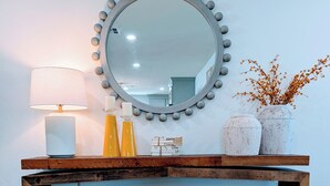 A wooden console table with a round mirror, two lamps, and decorative items.