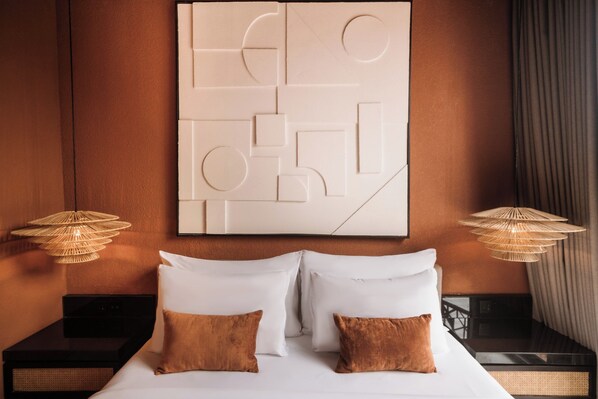 A hotel room with a large abstract wall art piece, a bed with white and brown pillows, and two wall-mounted lamps.