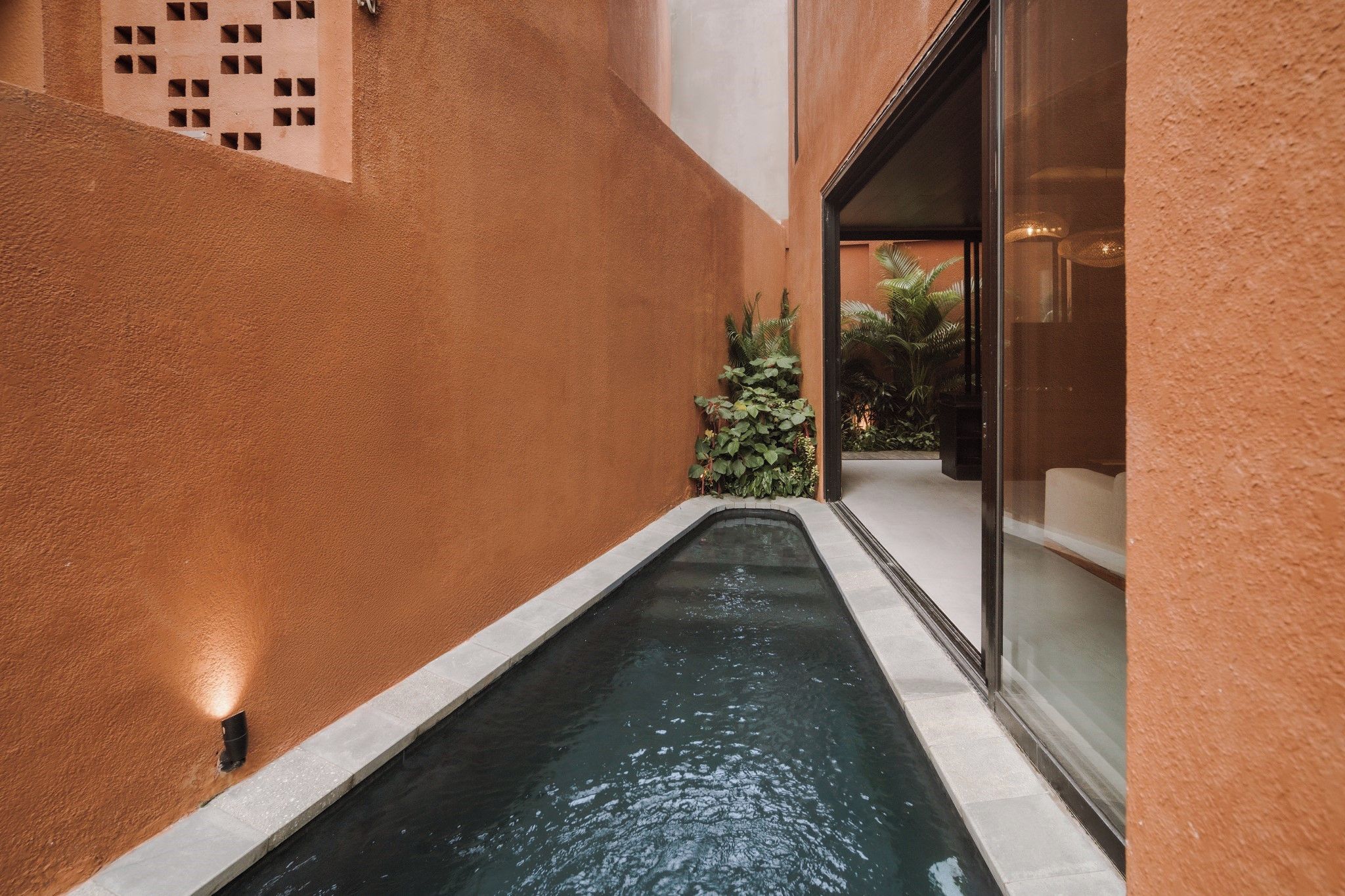 A narrow water feature with a tiled edge, surrounded by walls with a textured surface and a geometric pattern on one side.