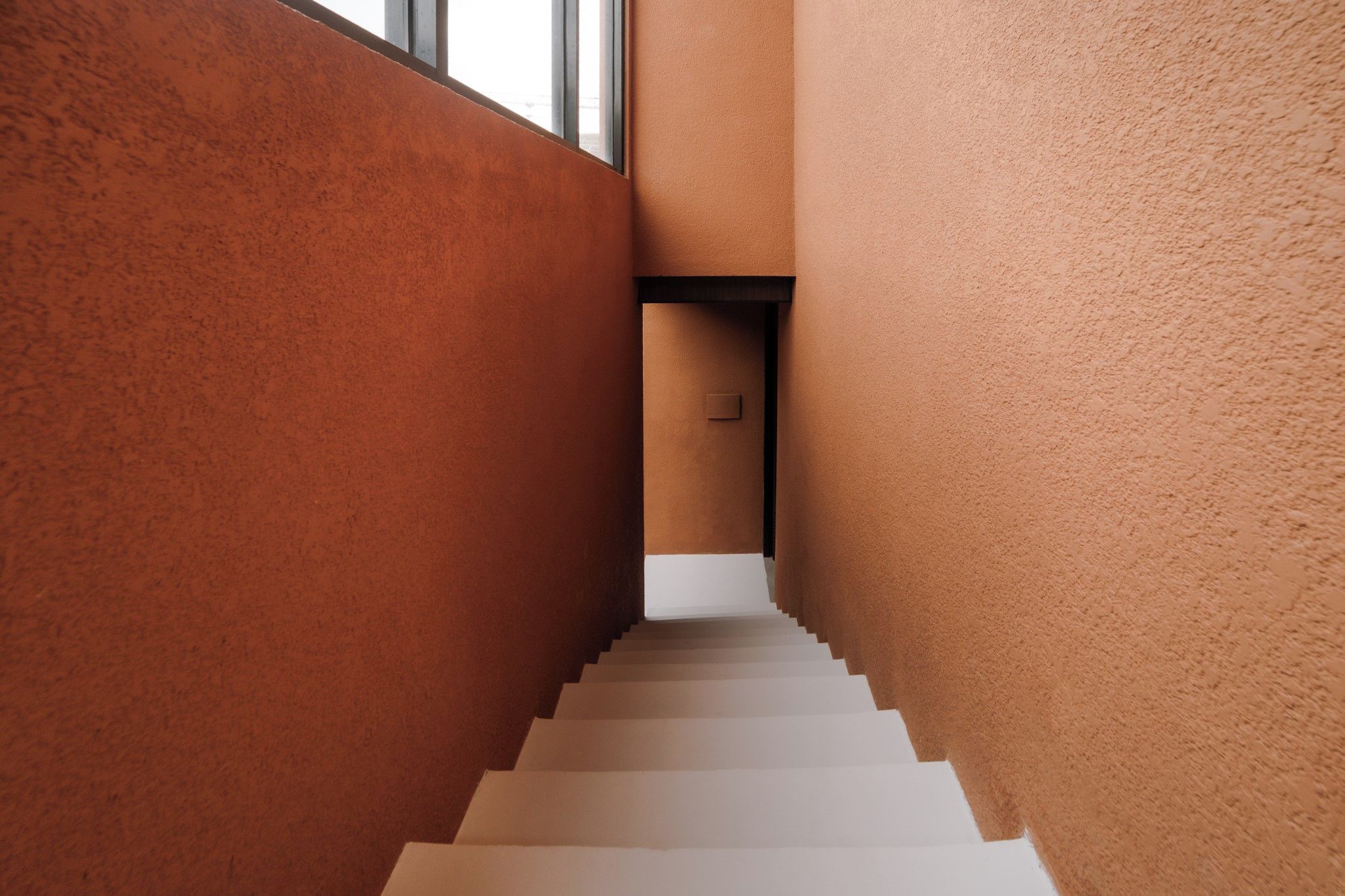 A staircase with a textured wall on one side and a plain wall on the other, leading to a door at the top.