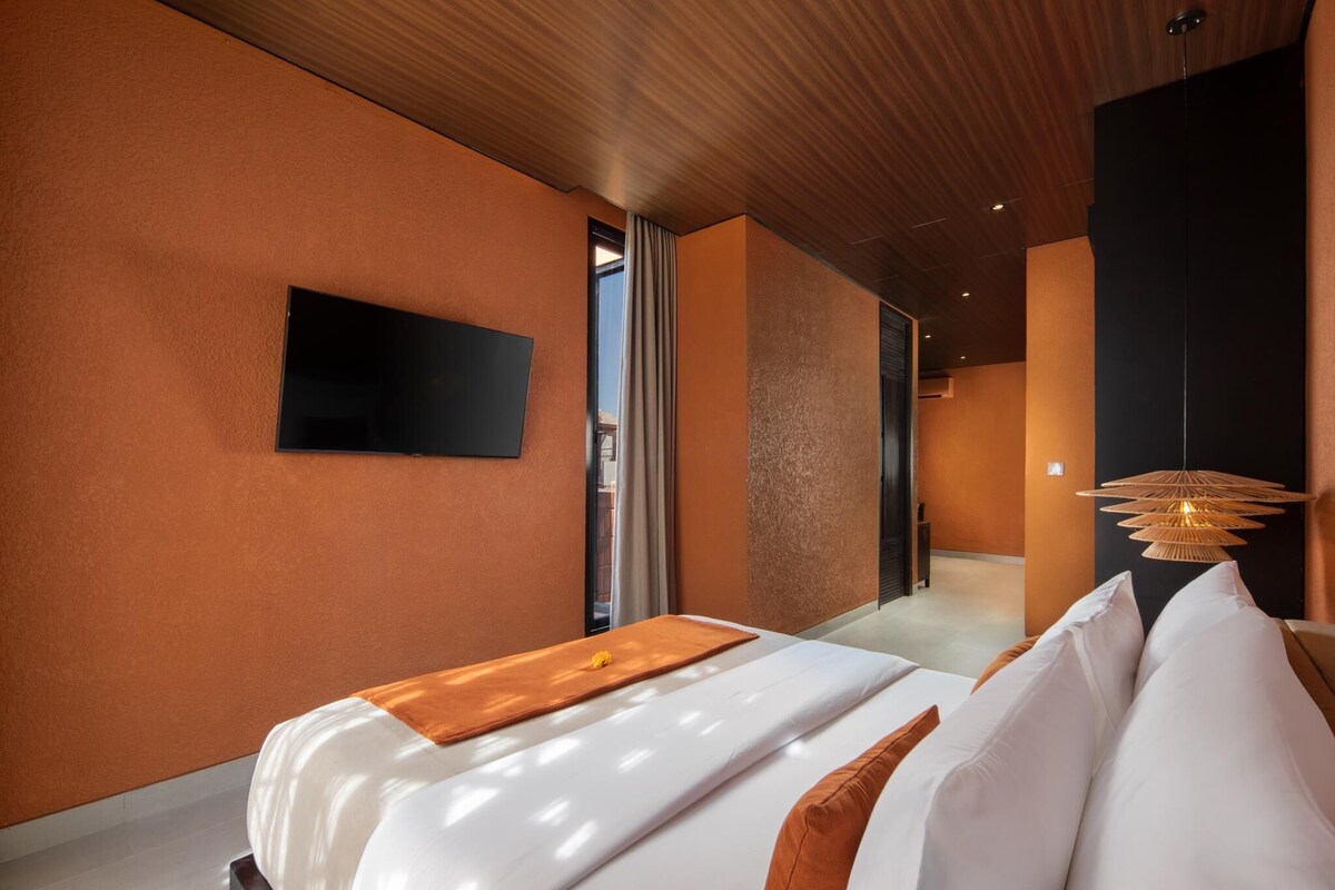 A modern hotel room with a large bed, a flat-screen TV, and a unique hanging light fixture.