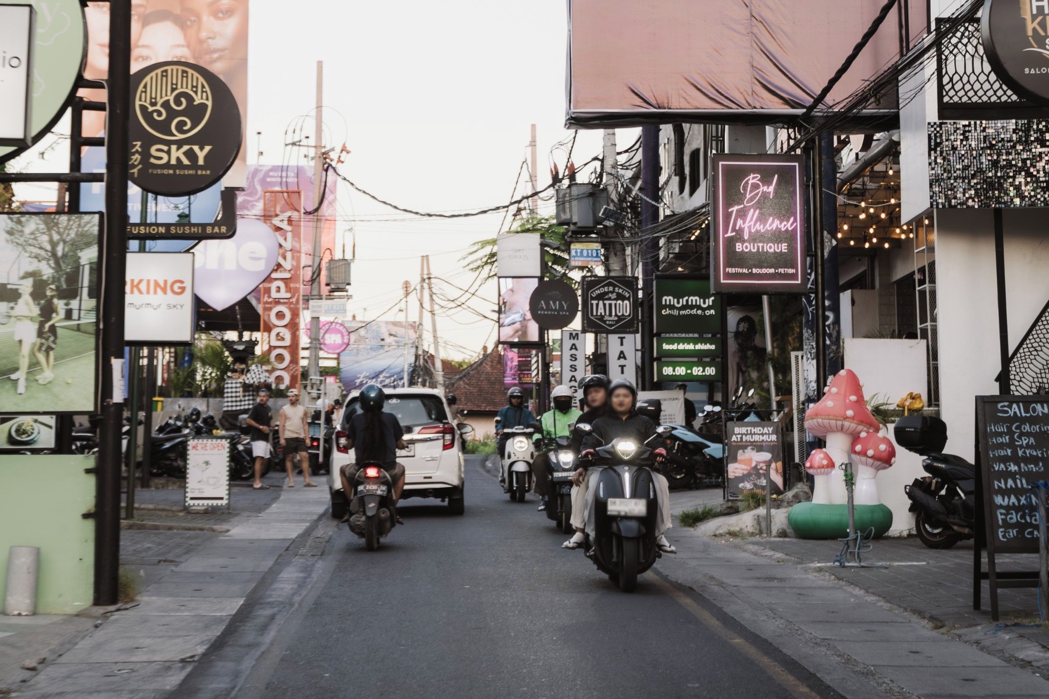 Une rue bordée de divers commerces et boutiques, notamment un bar à sushis et un salon de tatouage.