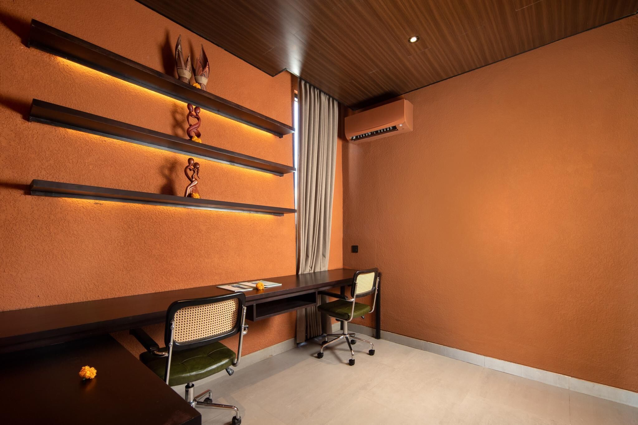 A conference room with a long table, two chairs, decorative wall shelves, and an air conditioning unit.