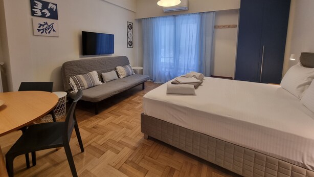 A modern hotel room with a bed, a sofa, a TV, and a dining area. - Acropolis Oasis  (Athens)