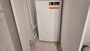 A compact laundry room with a white washing machine, a metal drying rack, and a small vent. - Acropolis Oasis  (Athens)