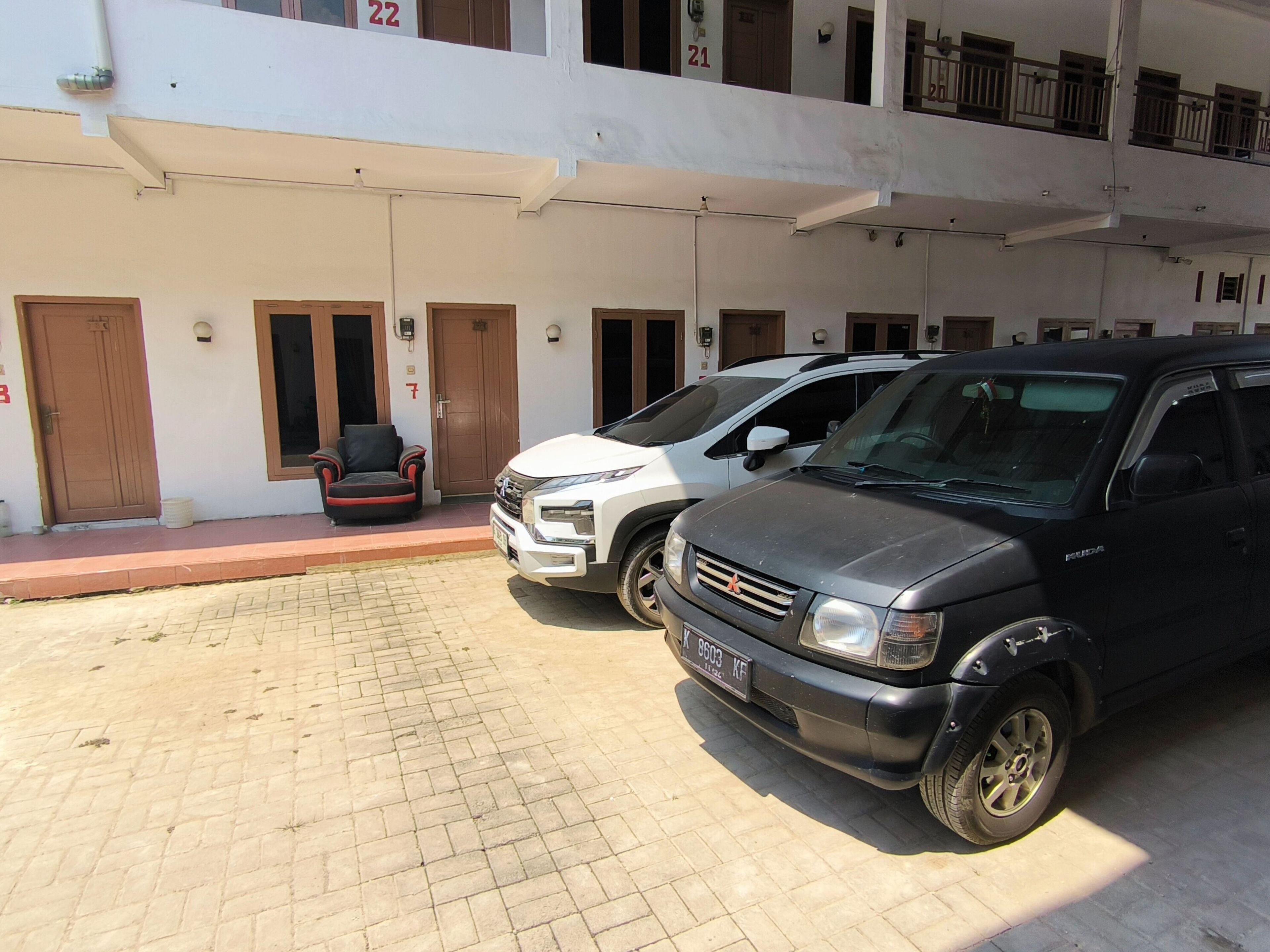 A building with numbered doors, a paved entrance, and parked cars.
