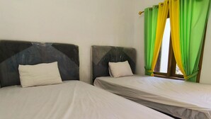 Two single beds with white linens, grey headboards, and a window with green and yellow curtains. - Trikora Guesthouse Syariah 1 (Pekalongan)