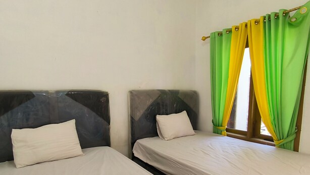 Two single beds with headboards, white bedding, and a window with green and yellow curtains. - Trikora Guesthouse Syariah 1 (Pekalongan)