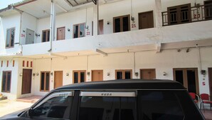 A multi-story building with numbered doors and windows, a covered parking area, and a black SUV parked in front. - Trikora Guesthouse Syariah 1 (Pekalongan)