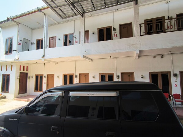 A multi-story building with numbered doors and windows, a covered parking area, and a black SUV parked in front. - Trikora Guesthouse Syariah 1 (Pekalongan)
