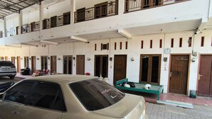 A multi-story building with numbered doors, a covered parking area, and a car parked in front. - Trikora Guesthouse Syariah 1 (Pekalongan)