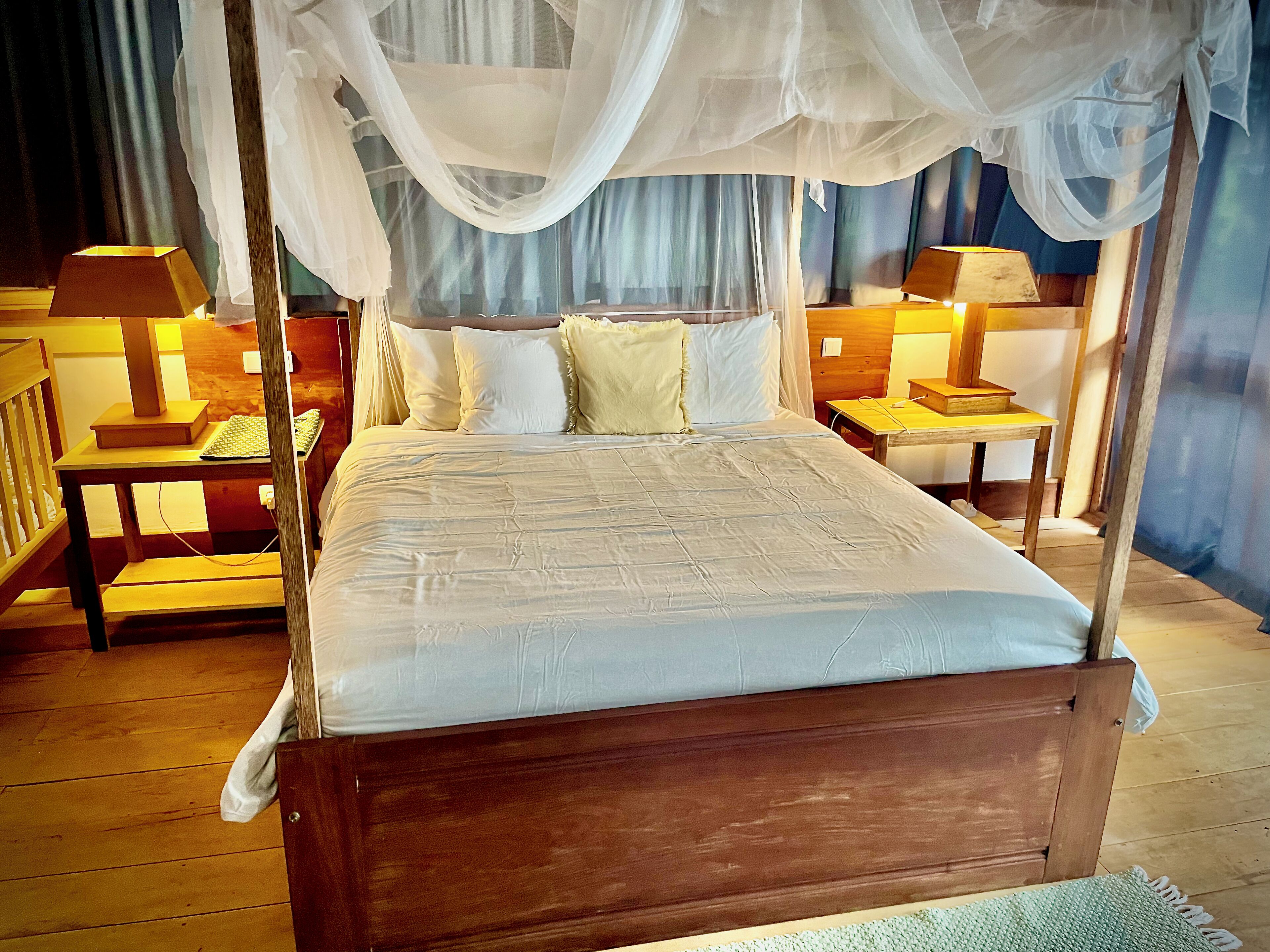 A four-poster bed with a canopy, two bedside tables with lamps, and a wooden floor.