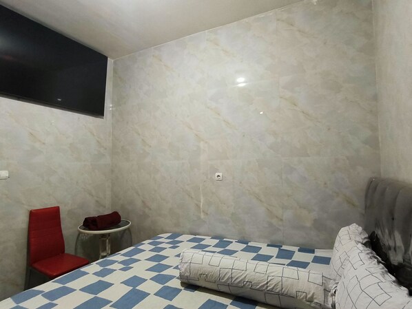 A small, modern room with a checkered bedspread, a red chair, and a small table. - Trikora Guesthouse Syariah 2 (Pekalongan)
