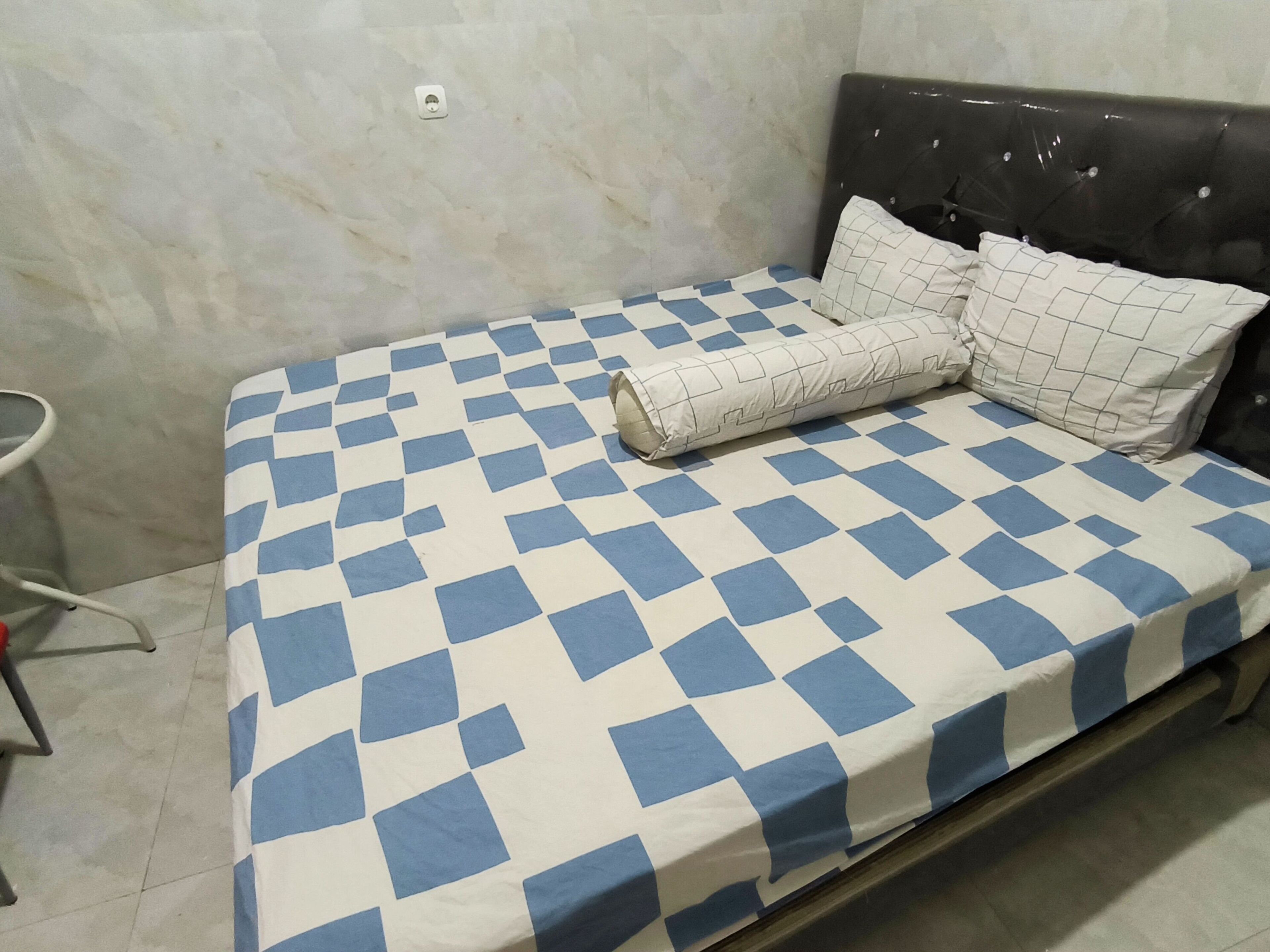 A bed with a checkered bedspread in a room with a marble wall and a simple headboard.