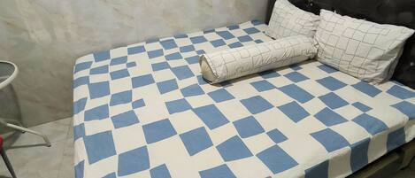 A bed with a checkered bedspread in a room with a marble wall and a simple headboard.