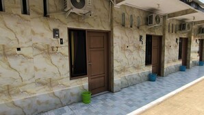 Un pasillo de hotel con paredes de mármol, puertas numeradas, unidades de aire acondicionado y piso de baldosas.