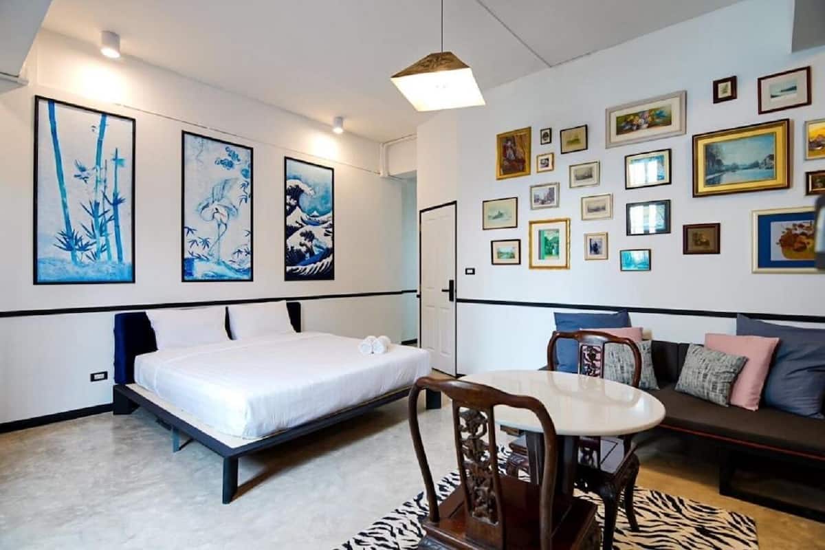 A hotel room with a bed, a dining table, and a sofa. There are multiple framed pictures on the walls.