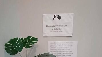 A corner with a potted plant, a white key box, and two signs on the wall.