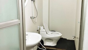 A small, compact bathroom with a toilet, a sink, and a shower. - The Character Yaowarat (Bangkok)
