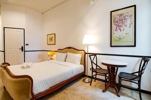 A hotel room with a bed, a bedside table with a lamp, a chair, and a framed picture on the wall. - The Character Yaowarat (Bangkok)
