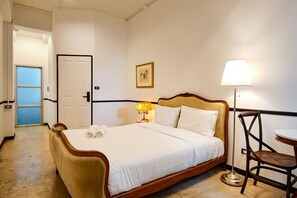 A hotel room with a bed, a bedside table with a lamp, a chair, and a door. - The Character Yaowarat (Bangkok)