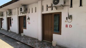 Een rij witte kamers met genummerde deuren, airconditioningsapparaten en een betegelde vloer.