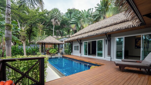 A wooden deck with a swimming pool, lounge chairs, and thatched-roof structures.