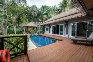Eine Holzterrasse mit Pool, Liegestühlen und strohgedeckten Gebäuden.