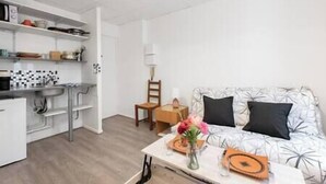 Un salon moderne et bien éclairé, avec un canapé, une table basse et un coin cuisine équipé d’un évier et d’étagères.