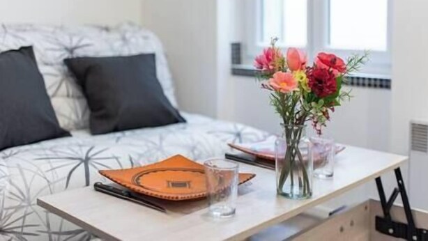 Une chambre à coucher bien rangée, avec un lit, une table de chevet sur laquelle se trouvent un carnet, un verre et un vase rempli de fleurs.